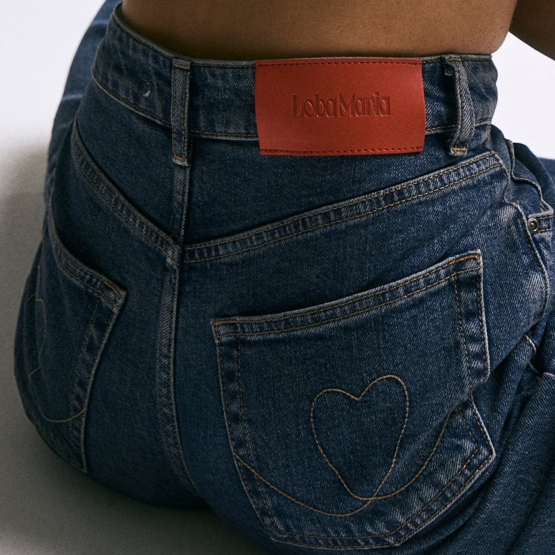 Blue jeans with a heart design on the pocket and a red belt, on a white background.